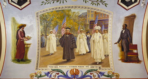 Allyn Cox's depiction (1973-4) of a 1917 New York suffrage parade is flanked by images of Rankin on the left and Joseph H.
Rainey (the first black man elected to the
U.S. House) on the right. This mural is part of the Great Experiment Hall in the Cox Corridors of the House wing of the Capitol and is not included on regular Capitol tours.

Credit: The Architect of the Capitol
